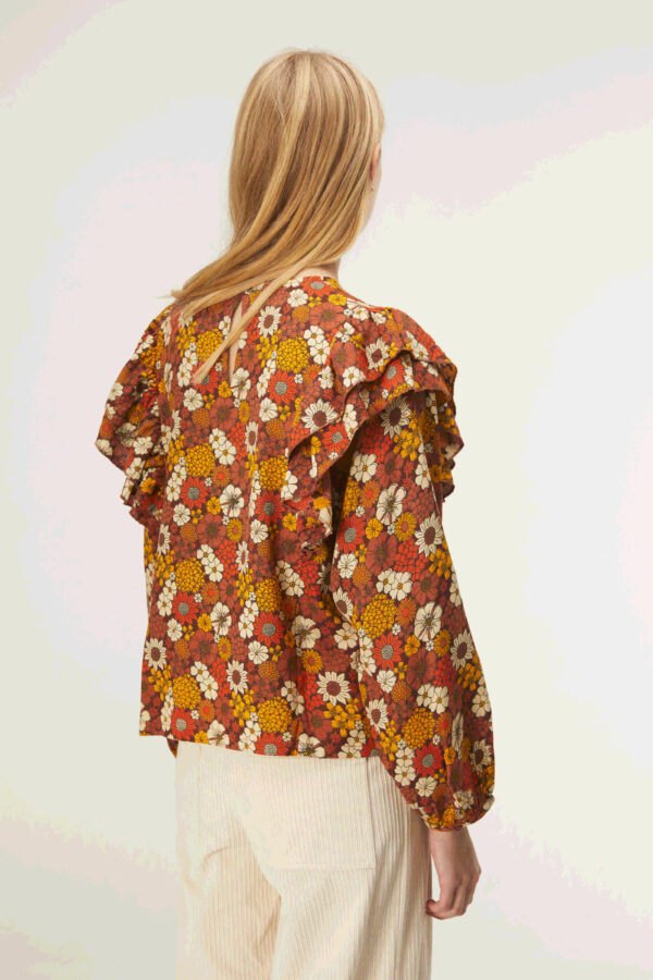 Back photo model wears orange floral blouse with ruffles